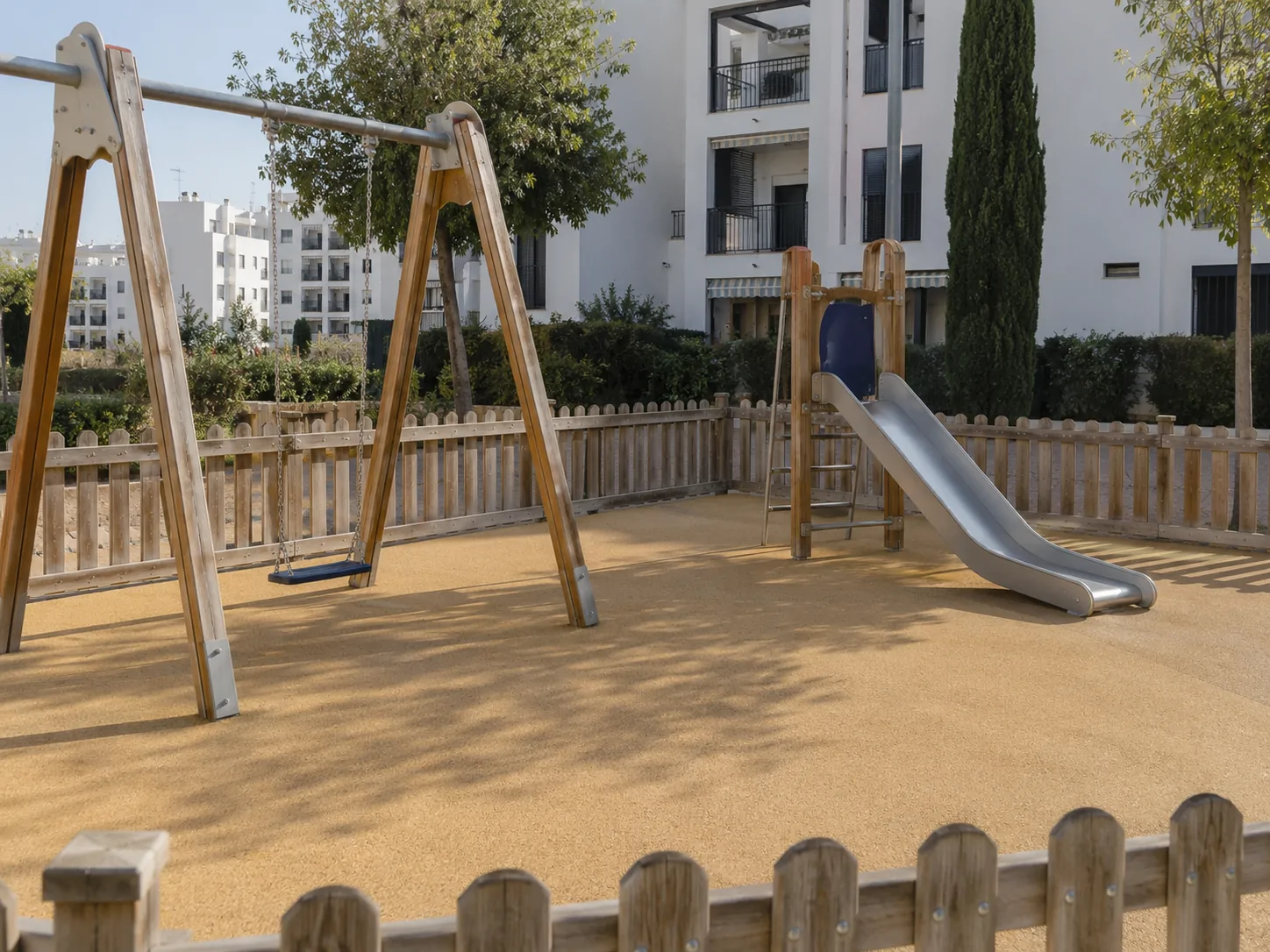 Zona infantil de una comunidad con suelo de caucho y columpios limpios